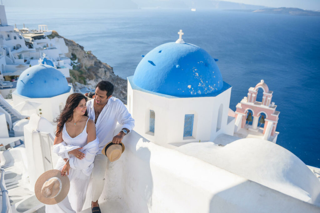 Couple in white on the steps of Oia beside the blue-domed churches of Santorini