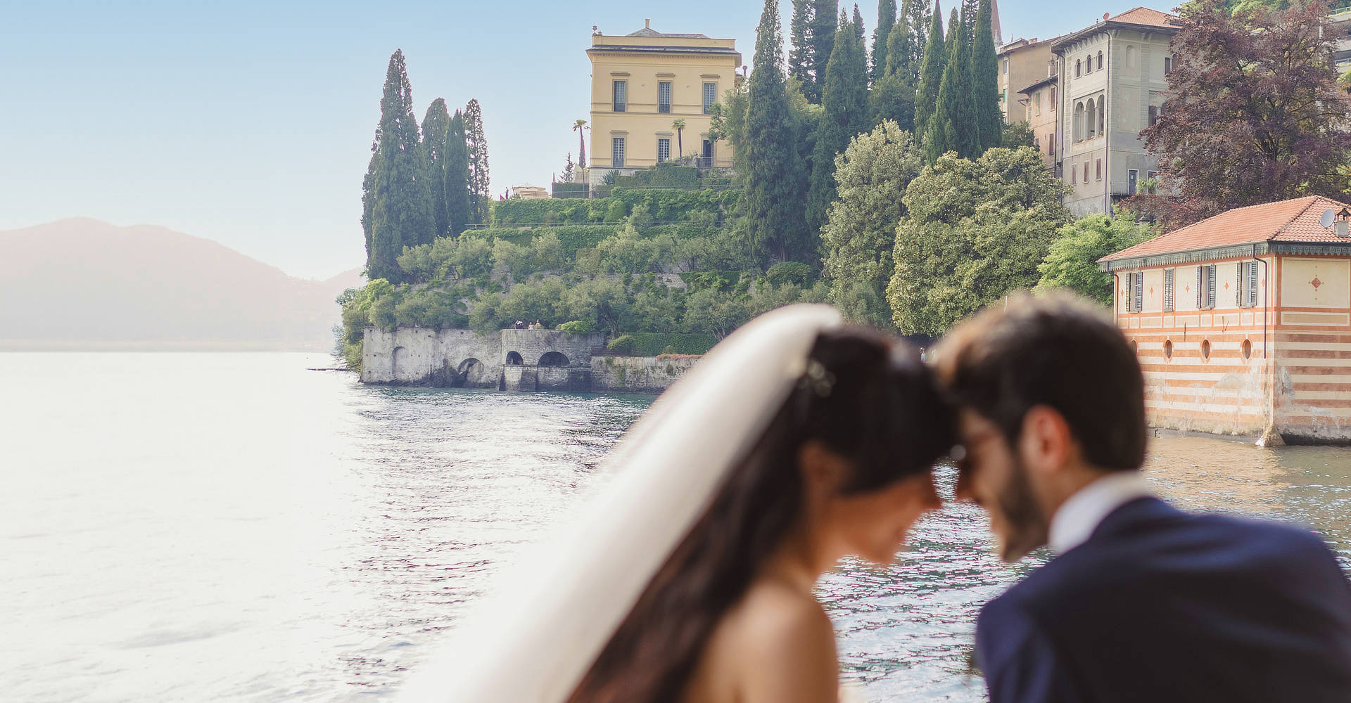 Bride and groom kiss on a boat in front of a very luxury house at lake Como