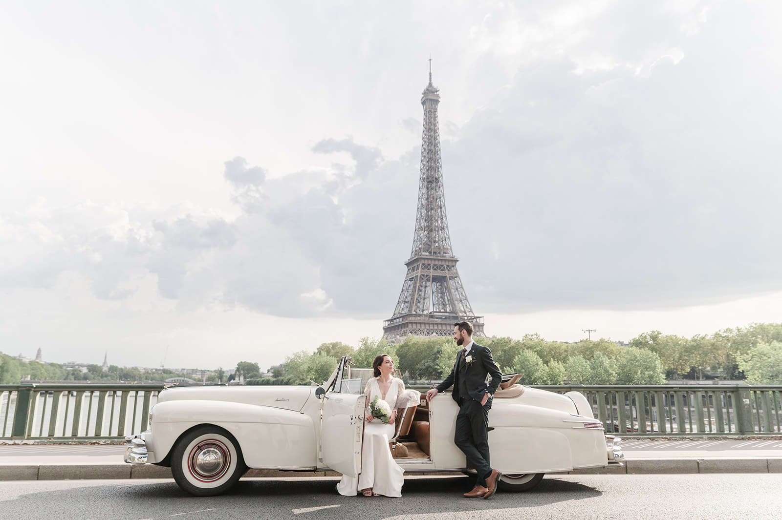 The bride and groom in a very relaxed pose with old vintage car over the river with the Eiffel