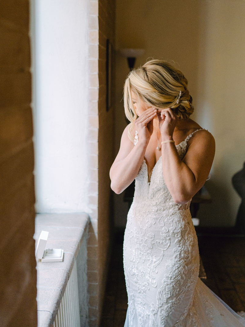 the bride puts her earrings in front of the window