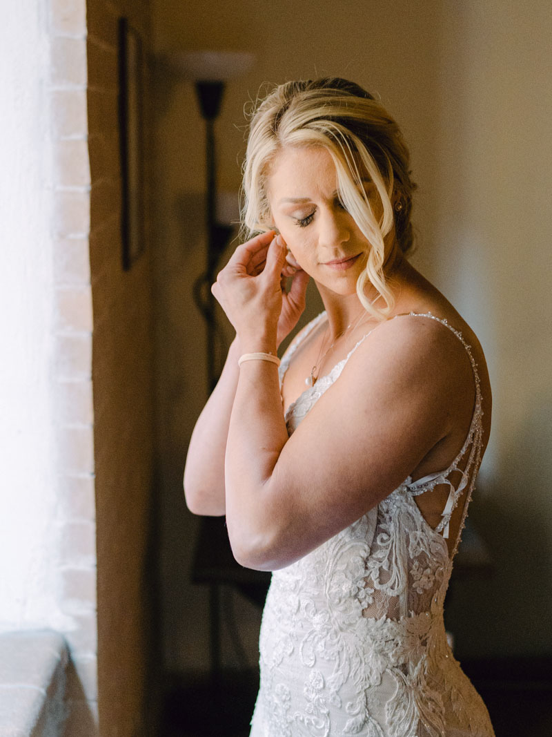 the bride puts her earrings in front of the window focused on doing that and smiling