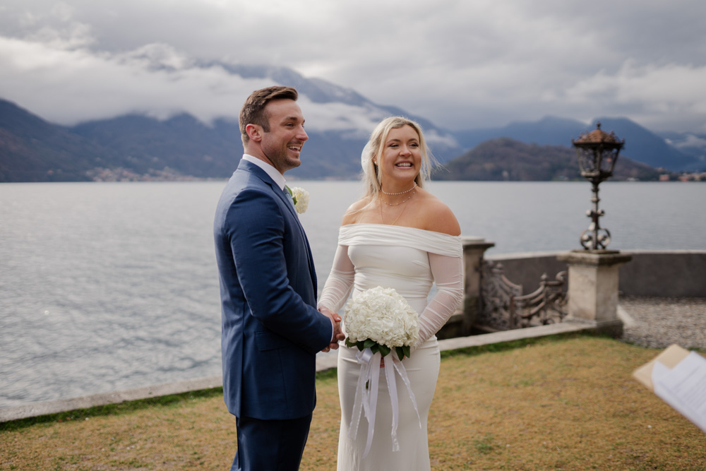 the day id cloudy with a lot of clouds over the mountain in the background. The couple smile to the celebrant during ceremony