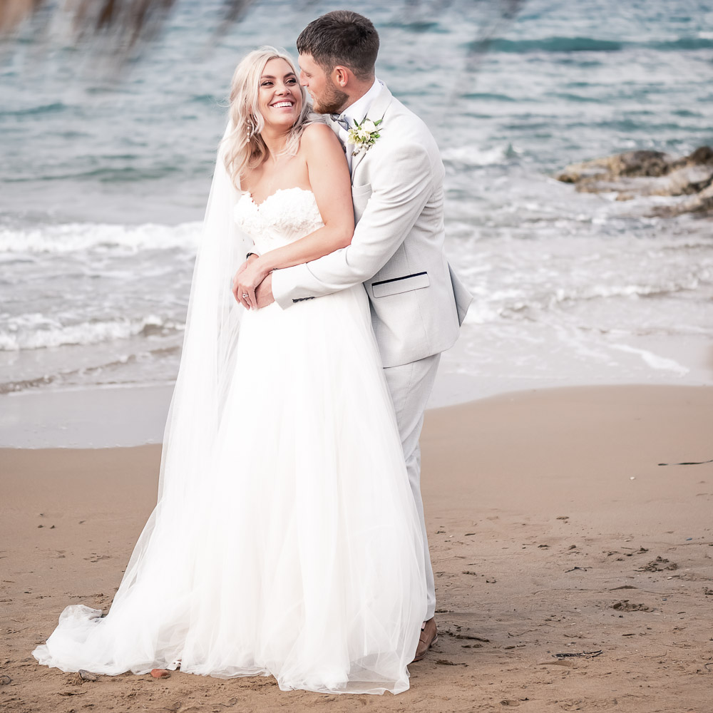 a love moment on the beach after their elopement ceremony, the groom is behind the bride and kiss her in the neck
