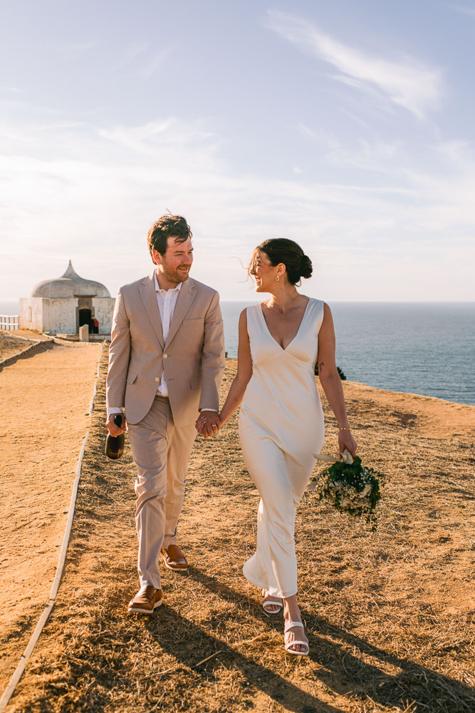 The couple walking with a Bottle of wine and the bouquet to celebrate their wedding in Sesimbra, Portugal