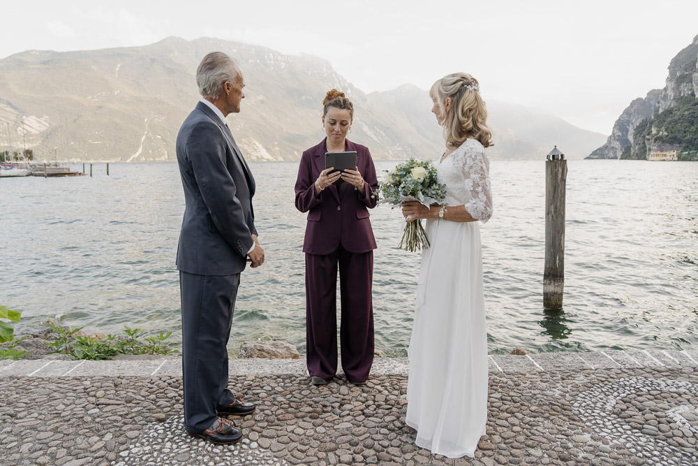 Vows renewal in lake Garda – 0004 The couple and the celebrant at the ceremony spot: on a pier over the lake with the mountains in the background, a bit foggy