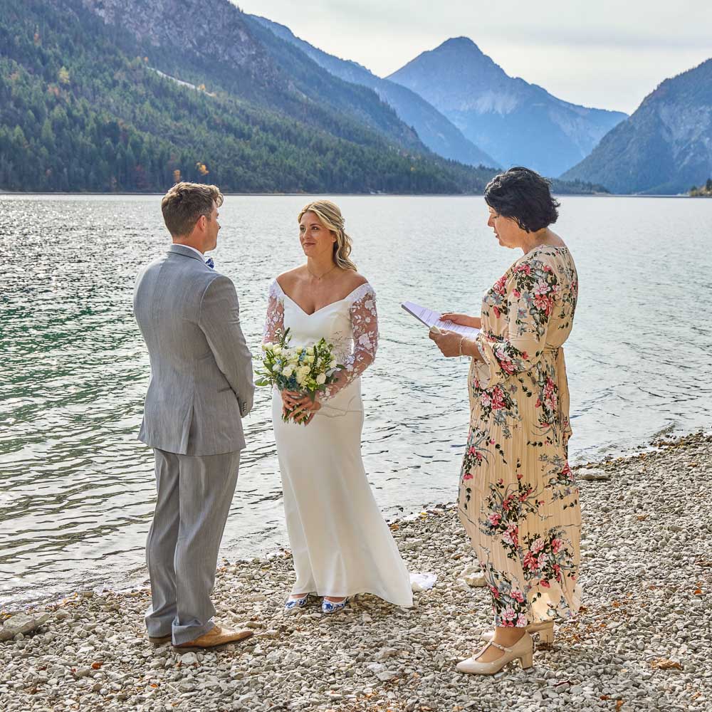 elopement wedding in Ambersee lake in Tyrol – 0002 elopement ceremony at Ambersee lake, tyrol. Th celebrant reads the text to the couple facing each other