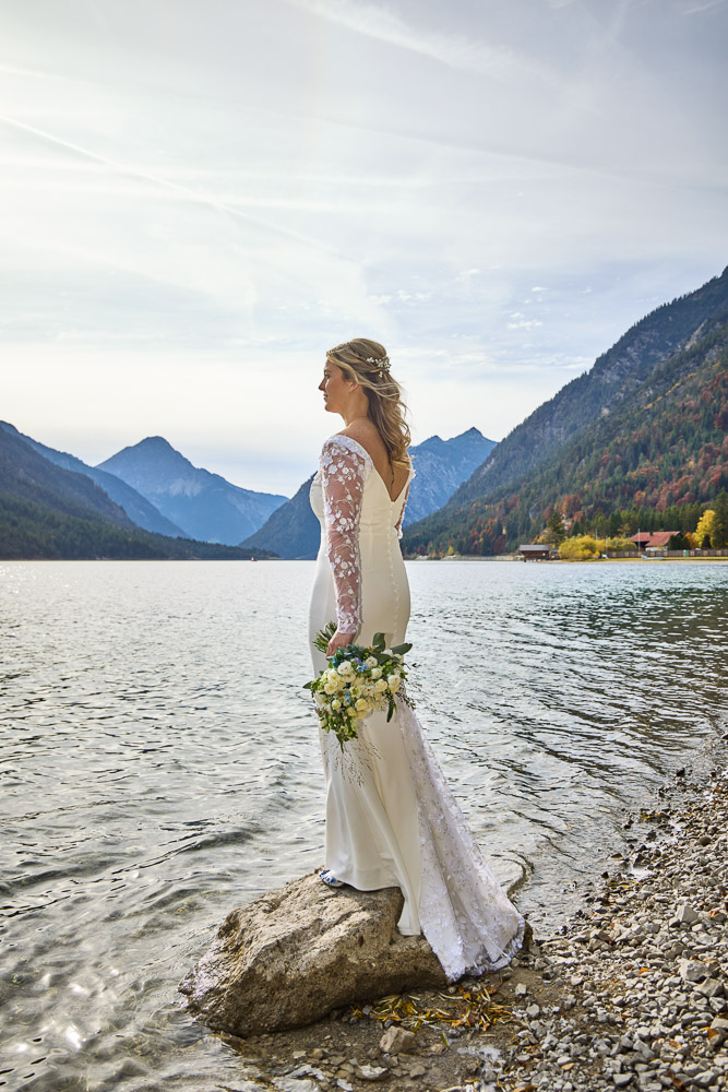 The bride back side with her bouquet, the lake as backdrop in Austria