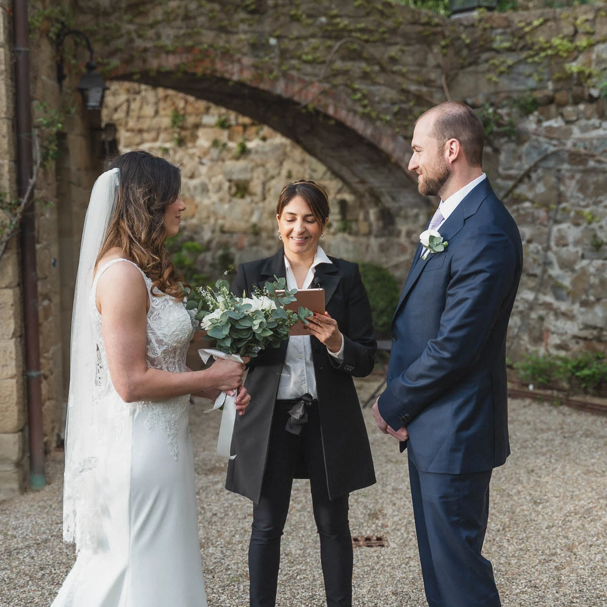 Celebrant officiating an intimate elopement ceremony under a stone arch at a Tuscan villa