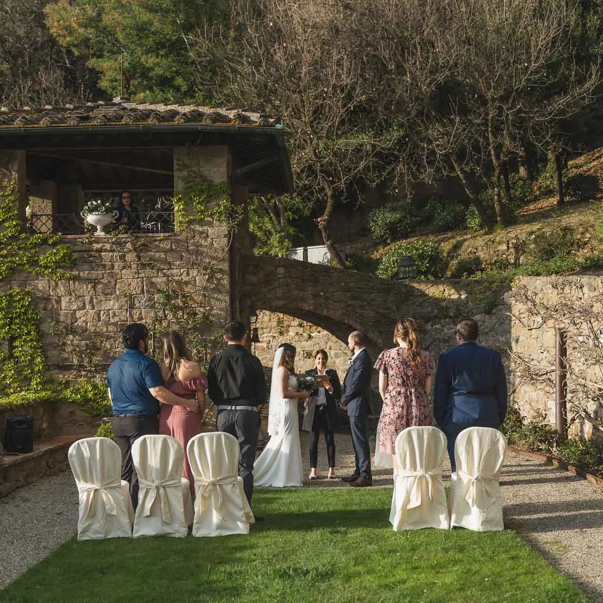 Intimate micro wedding ceremony in a stone-walled garden at a private Tuscan villa with a small group of guests