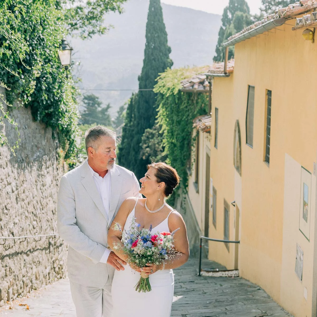 Couple celebrating their vow renewal in a charming Tuscan village alley surrounded by cypress trees