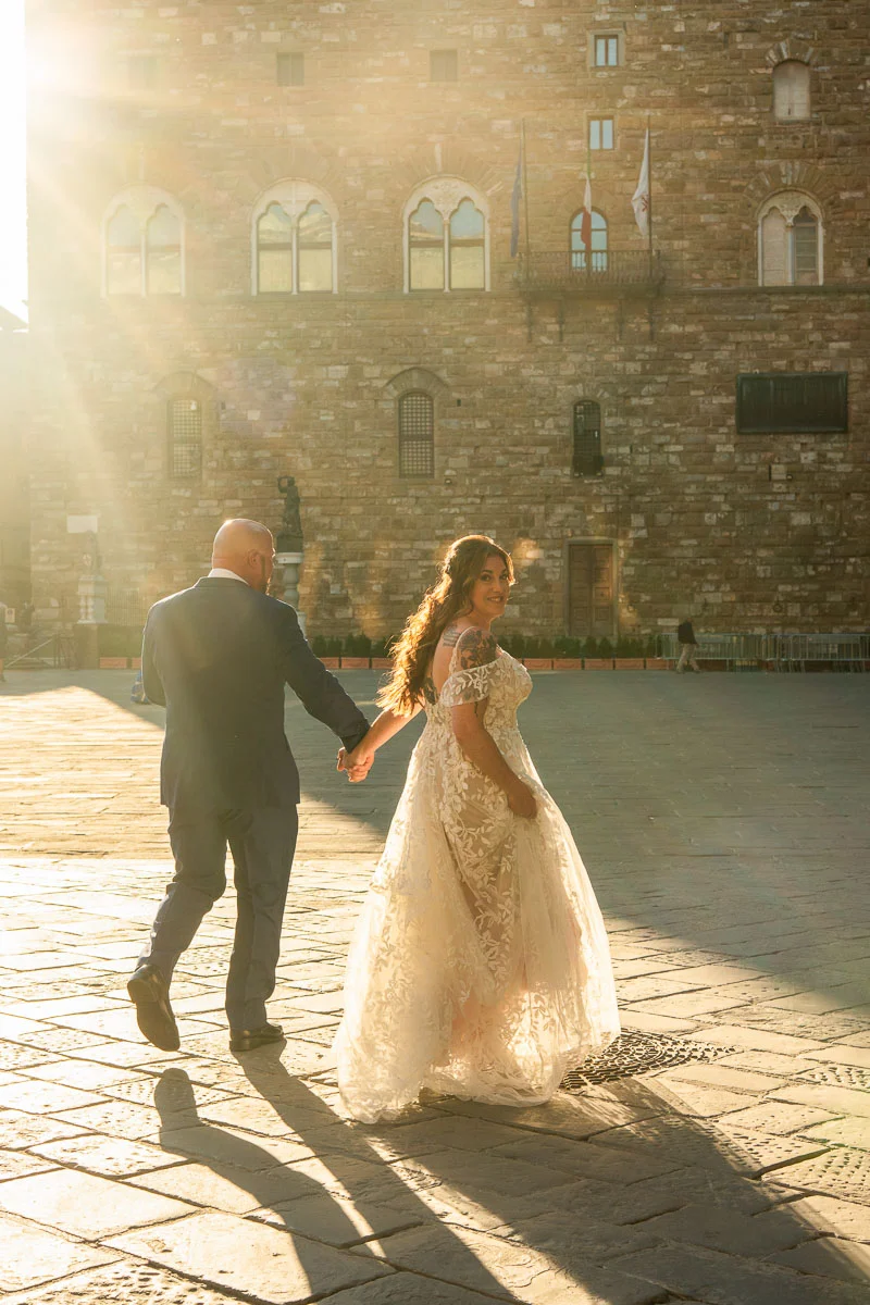 elopment at Fiesole, Tuscany-01 Couple eloping in Florence at golden hour, bride in lace gown and groom in navy suit walking hand in hand across Piazza della Signoria