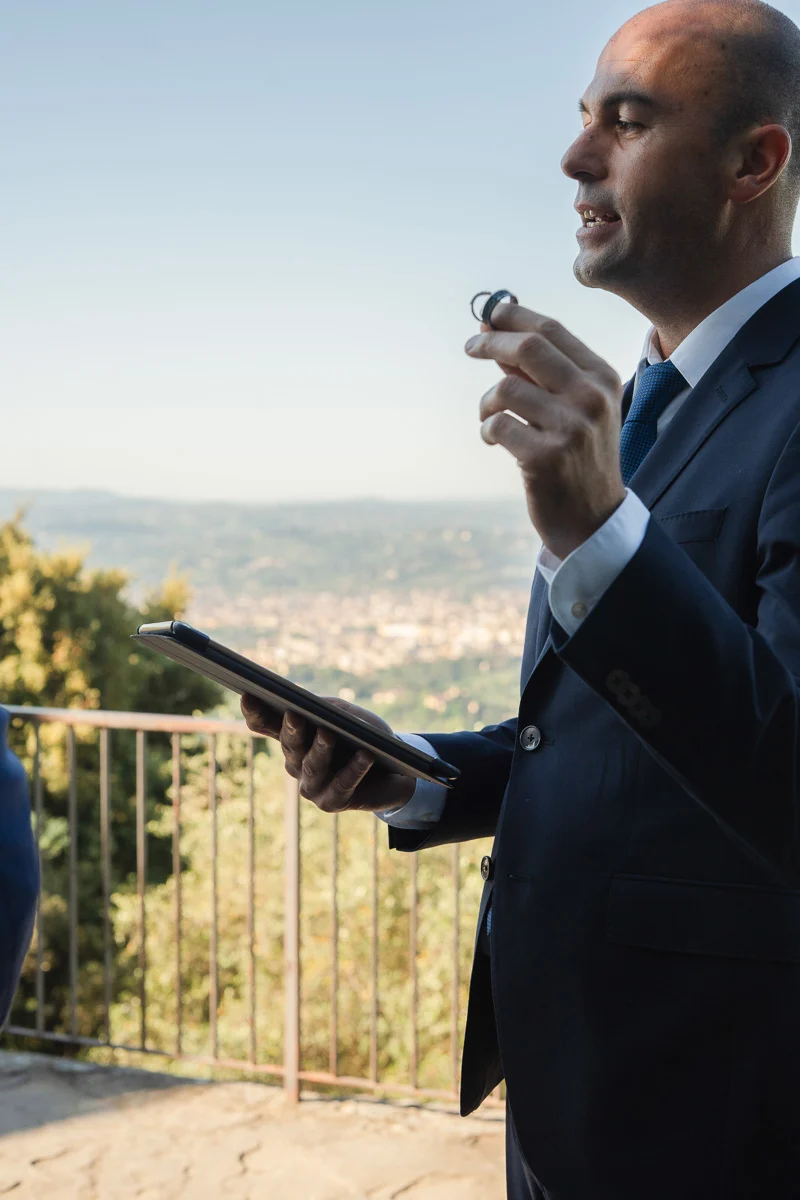 elopment at Fiesole, Tuscany-12 Wedding celebrant holding up the rings during an elopement ceremony on a hilltop terrace in Fiesole, with the Tuscan landscape behind