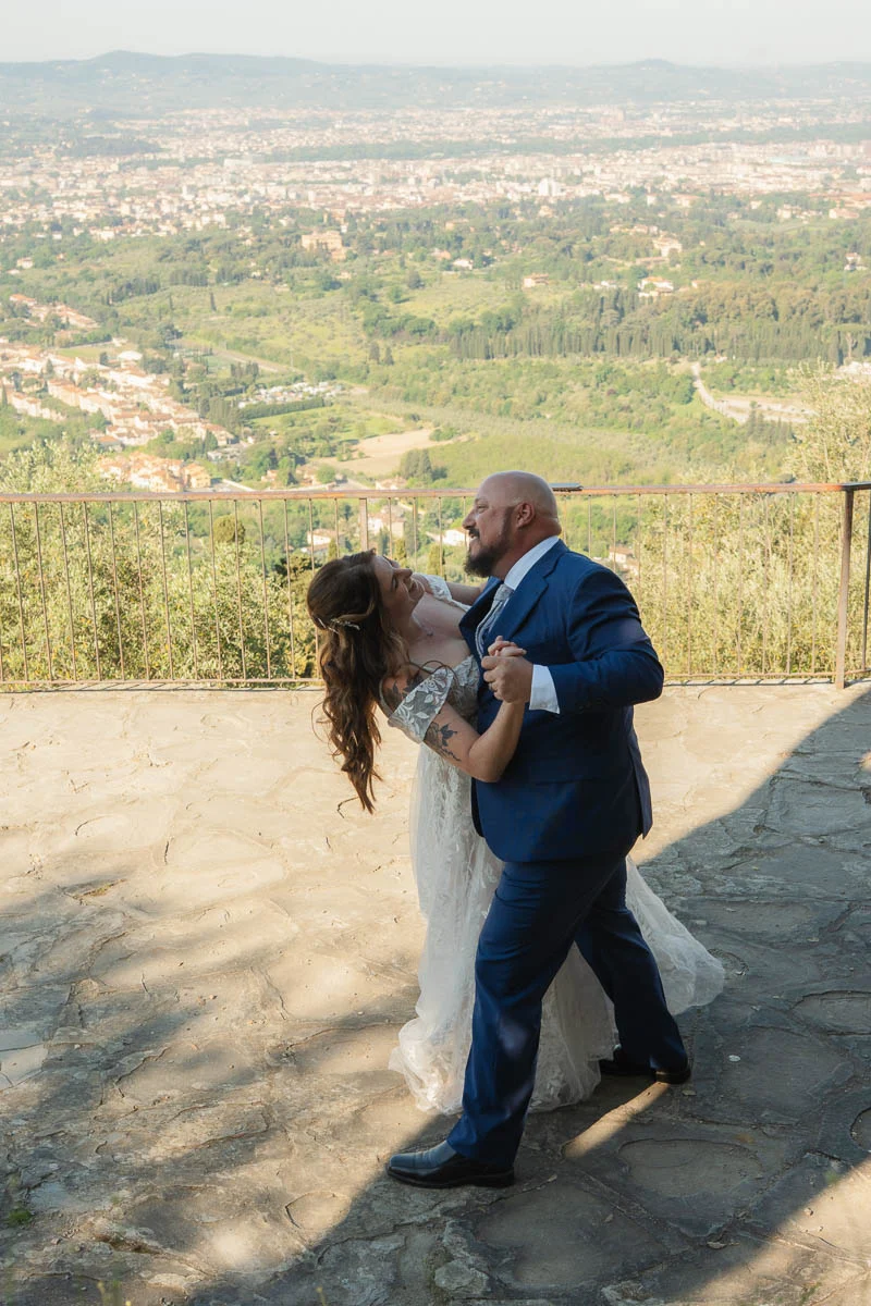 elopment at Fiesole, Tuscany-19 Bride and groom dancing joyfully on a stone terrace in Fiesole after their elopement, with the panoramic Tuscany landscape stretching behind them