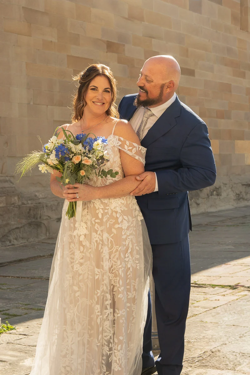 elopment at Fiesole, Tuscany-25 Smiling newlyweds posing together in front of a historic stone church in Fiesole, Tuscany, after their intimate elopement