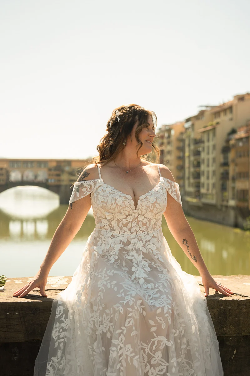 elopment at Fiesole, Tuscany-26 Bride in lace off-shoulder wedding dress posing on a bridge with the Ponte Vecchio and the Arno River in the background, Florence