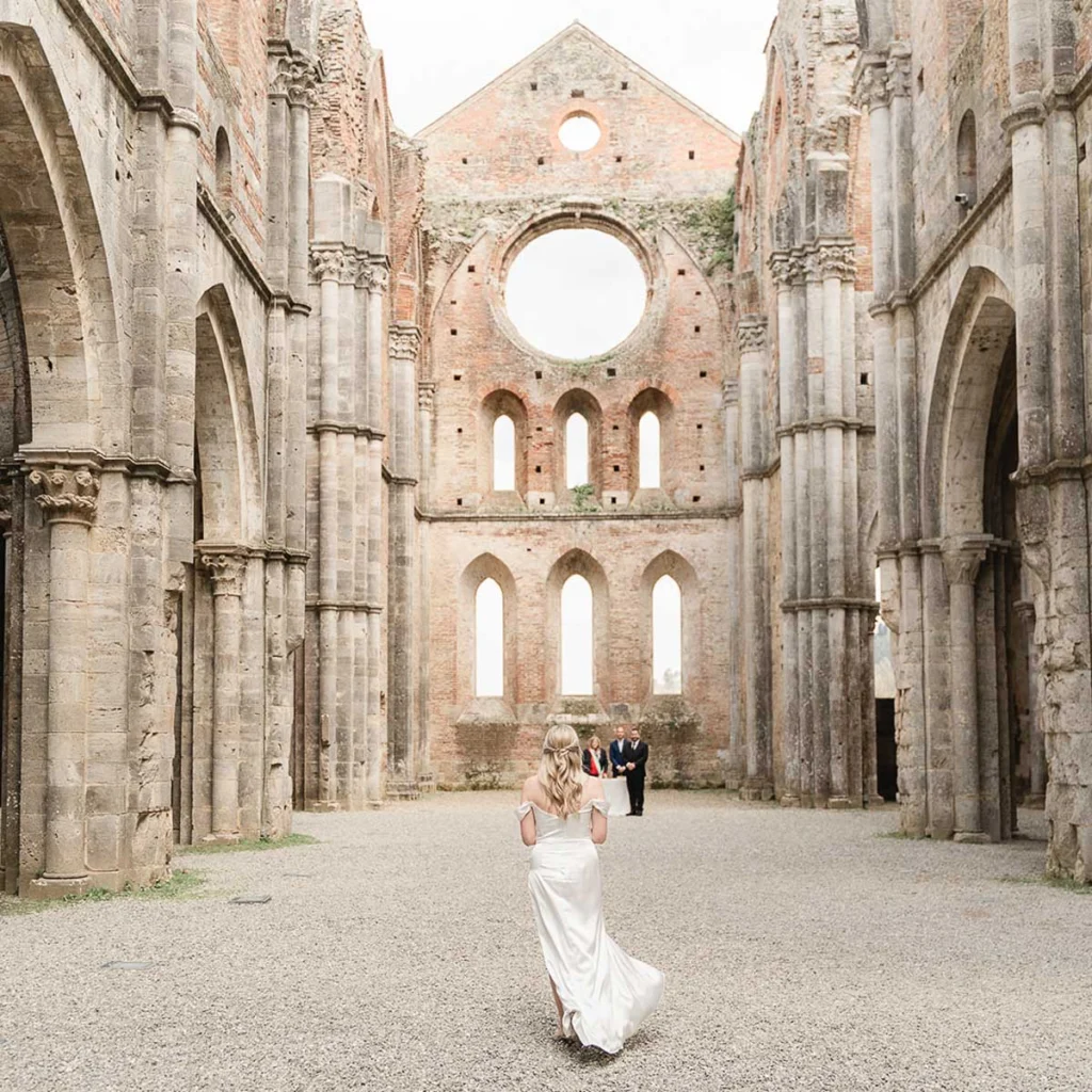 Bride walking towards ceremony at San Galgano Abbey ruins, Tuscany