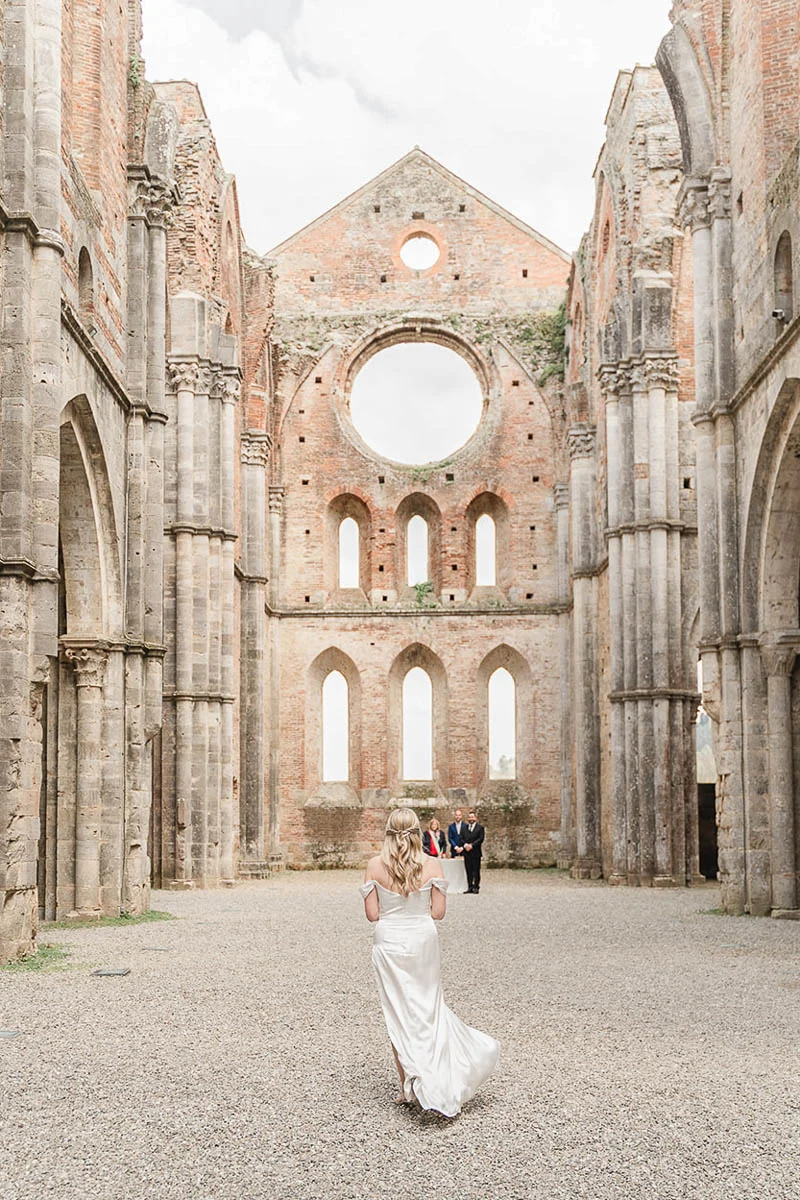 Bride walking down the roofless nave of San Galgano Abbey during her elopement ceremony