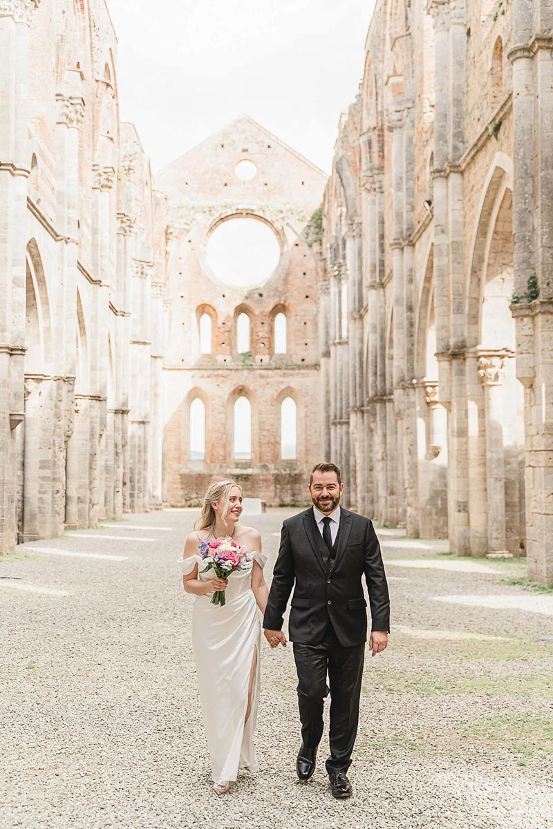 Newlyweds walking hand in hand through the nave of San Galgano Abbey, Tuscany