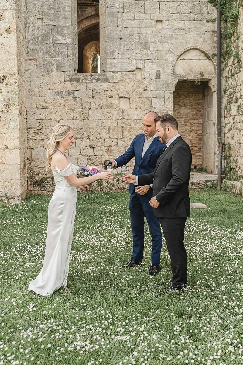 elopment wedding in Tuscany-San Galgano-37 Bride and groom sharing champagne in a wildflower meadow outside San Galgano Abbey