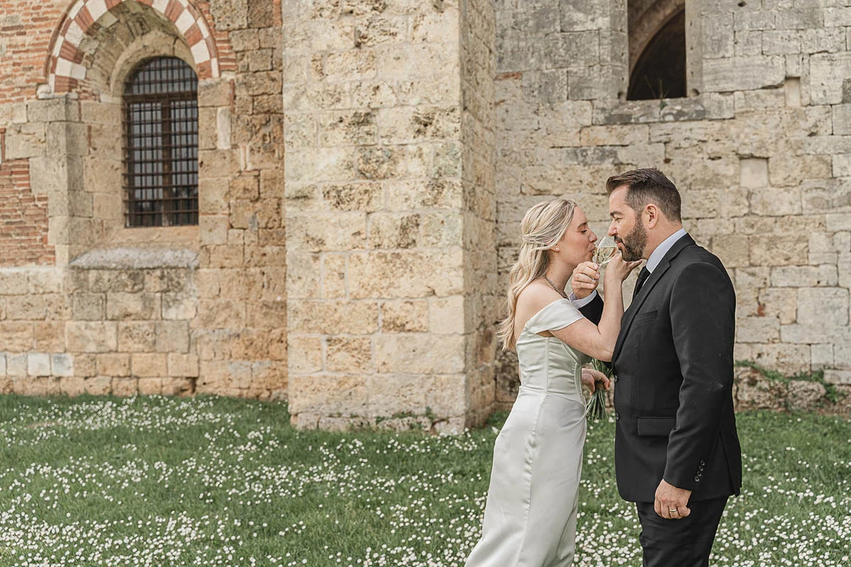 elopment wedding in Tuscany-San Galgano-38 Newlyweds toasting with champagne in a wildflower meadow beside San Galgano Abbey, Tuscany