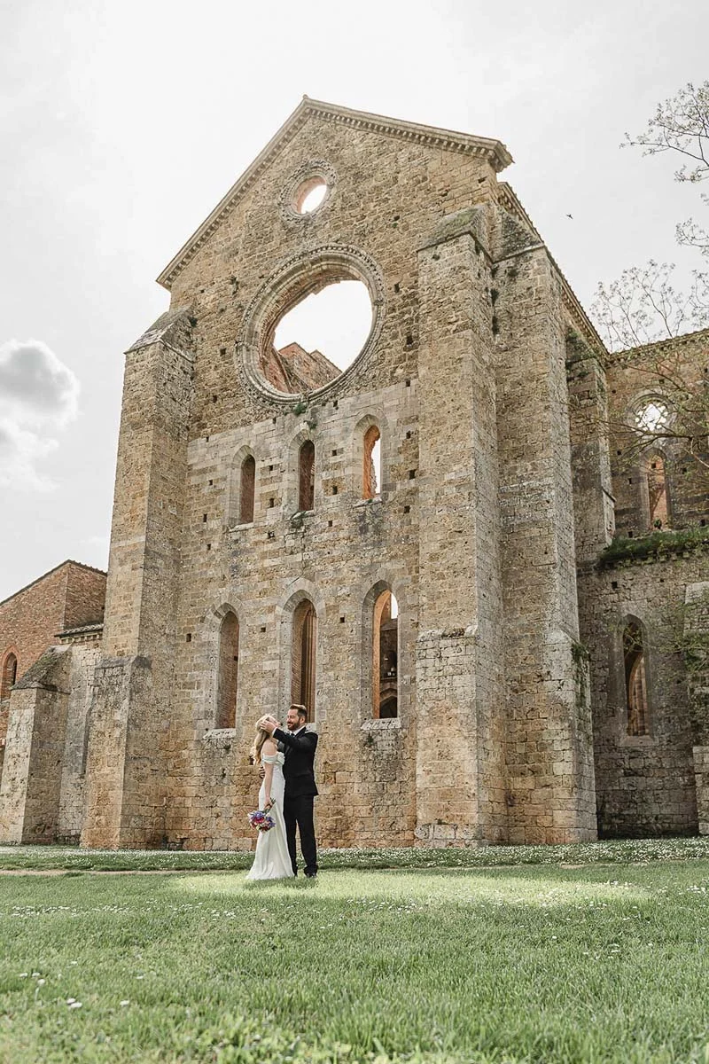 Newlyweds embracing in front of the facade of San Galgano Abbey, Tuscany