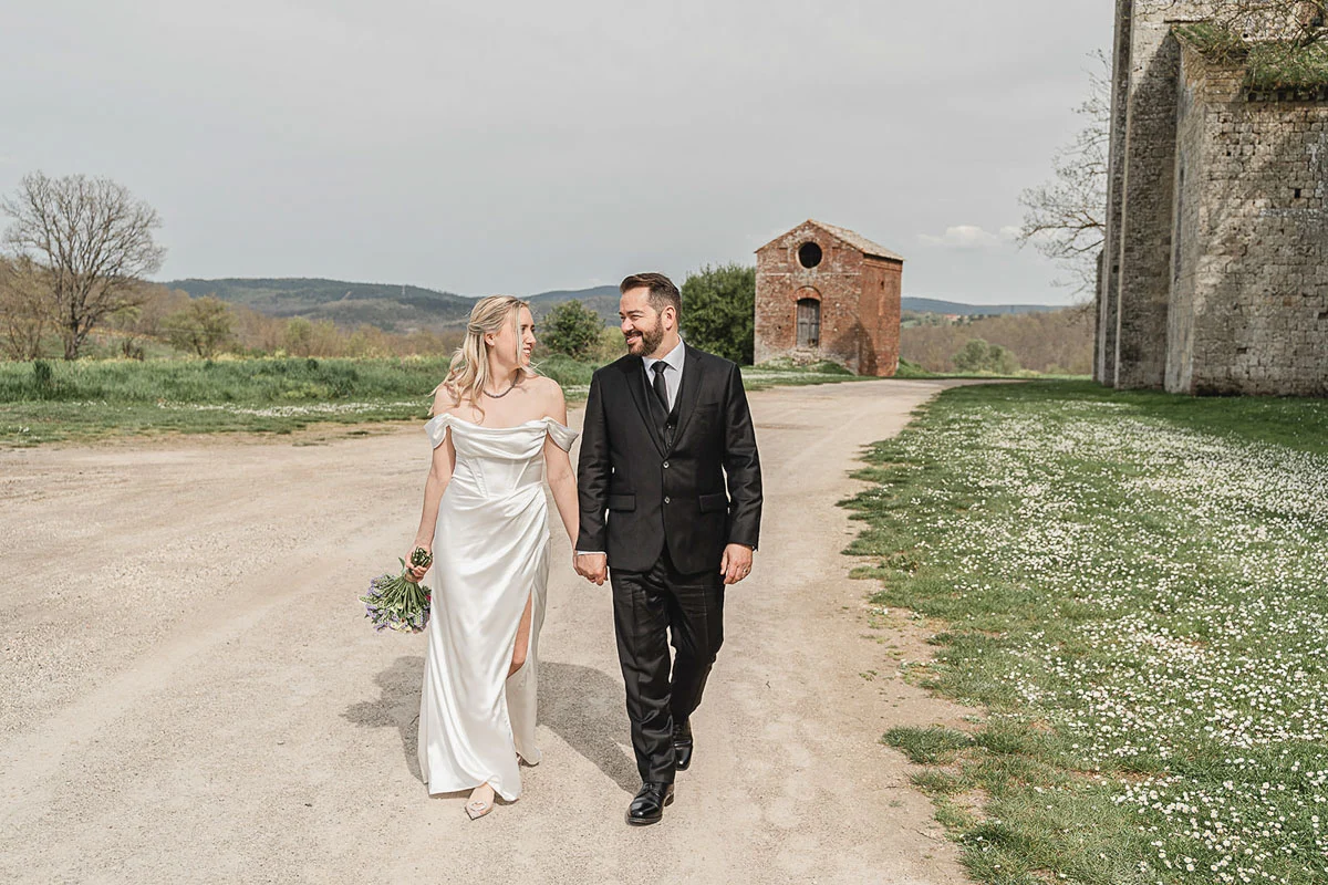 elopment wedding in Tuscany-San Galgano-41 Couple strolling past the chapel ruins of San Galgano with open Tuscan countryside behind them