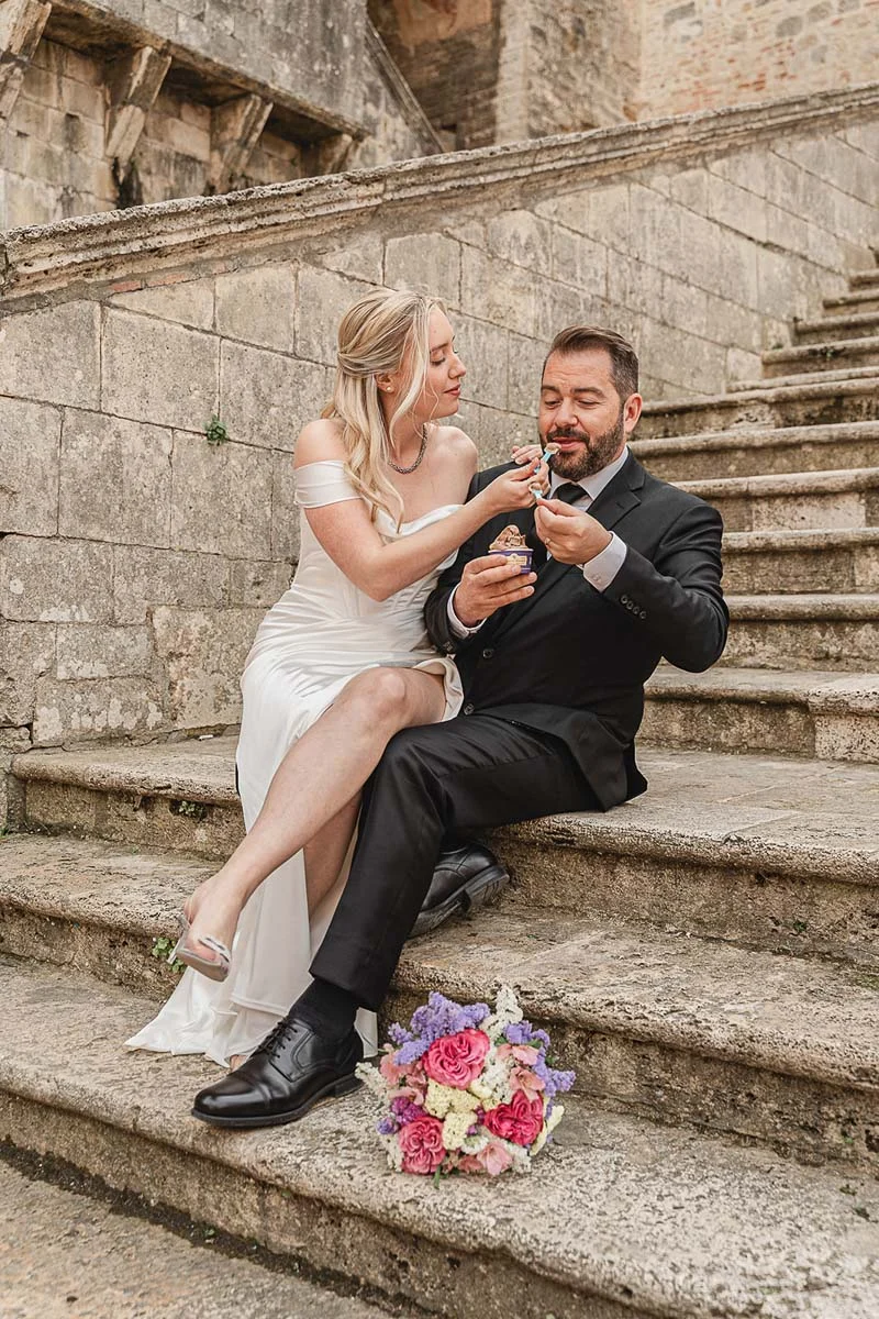 Bride and groom sitting on the abbey steps sharing a treat after their elopement, San Galgano