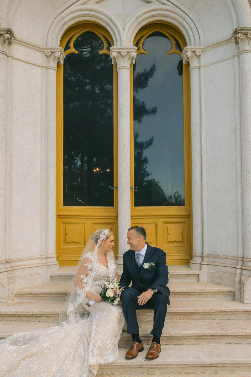 Ethan and Jennifer sitting on the palace steps beneath the Gothic arched windows of Biester Palace