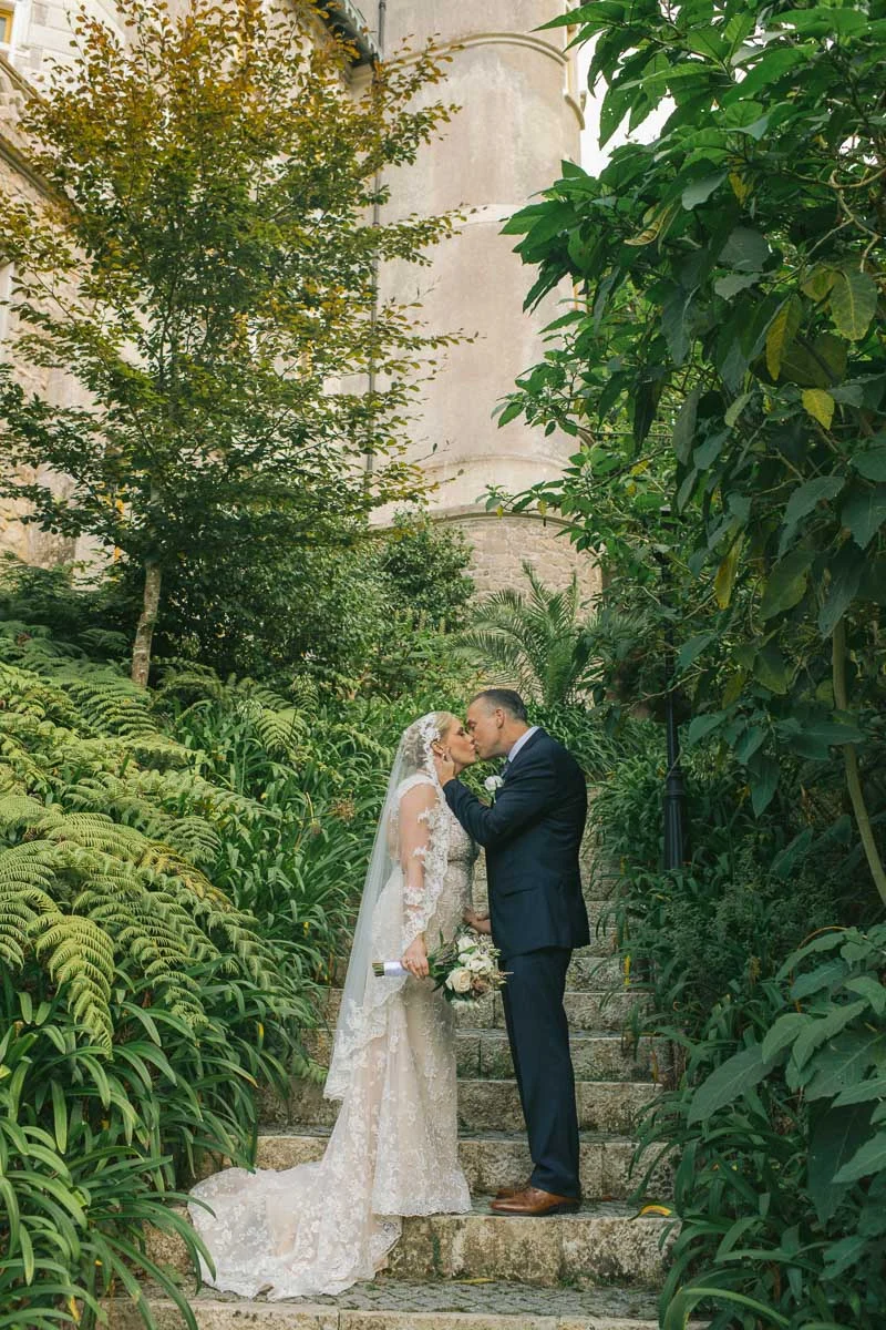 Bride and groom kissing on the garden steps surrounded by lush greenery at Biester Palace
